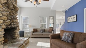 A living room with a stone fireplace, a brown sofa, and a blue accent wall. - Charming Lakefront House Near Shorty Pants at 21mm (Osage Beach)