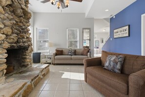 A living room with a stone fireplace, a brown sofa, and a blue accent wall. - Charming Lakefront House Near Shorty Pants at 21mm (Osage Beach)