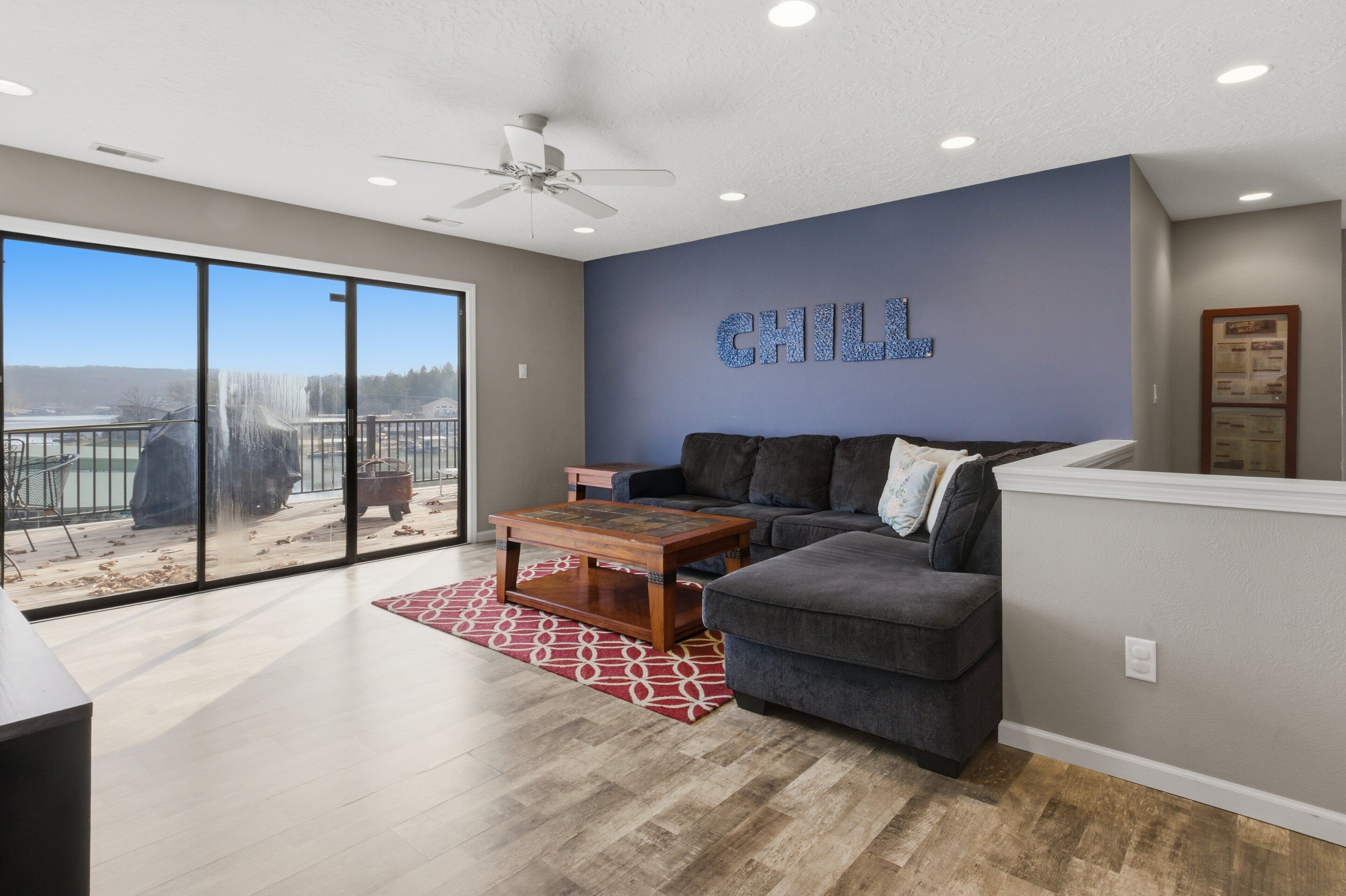 A spacious living room with a gray couch, a wooden coffee table, and a large window offering a view of a waterfall.