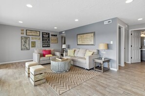 A spacious living room with a large grey sofa, a coffee table, and a patterned rug. - Lakefront Home w/ Decks & Docks at Shorty Pants Bar 21mm (Osage Beach)
