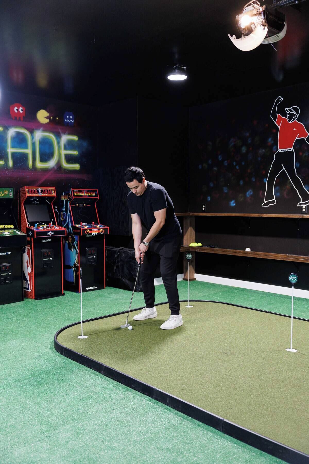 A person playing golf indoors with arcade games in the background.