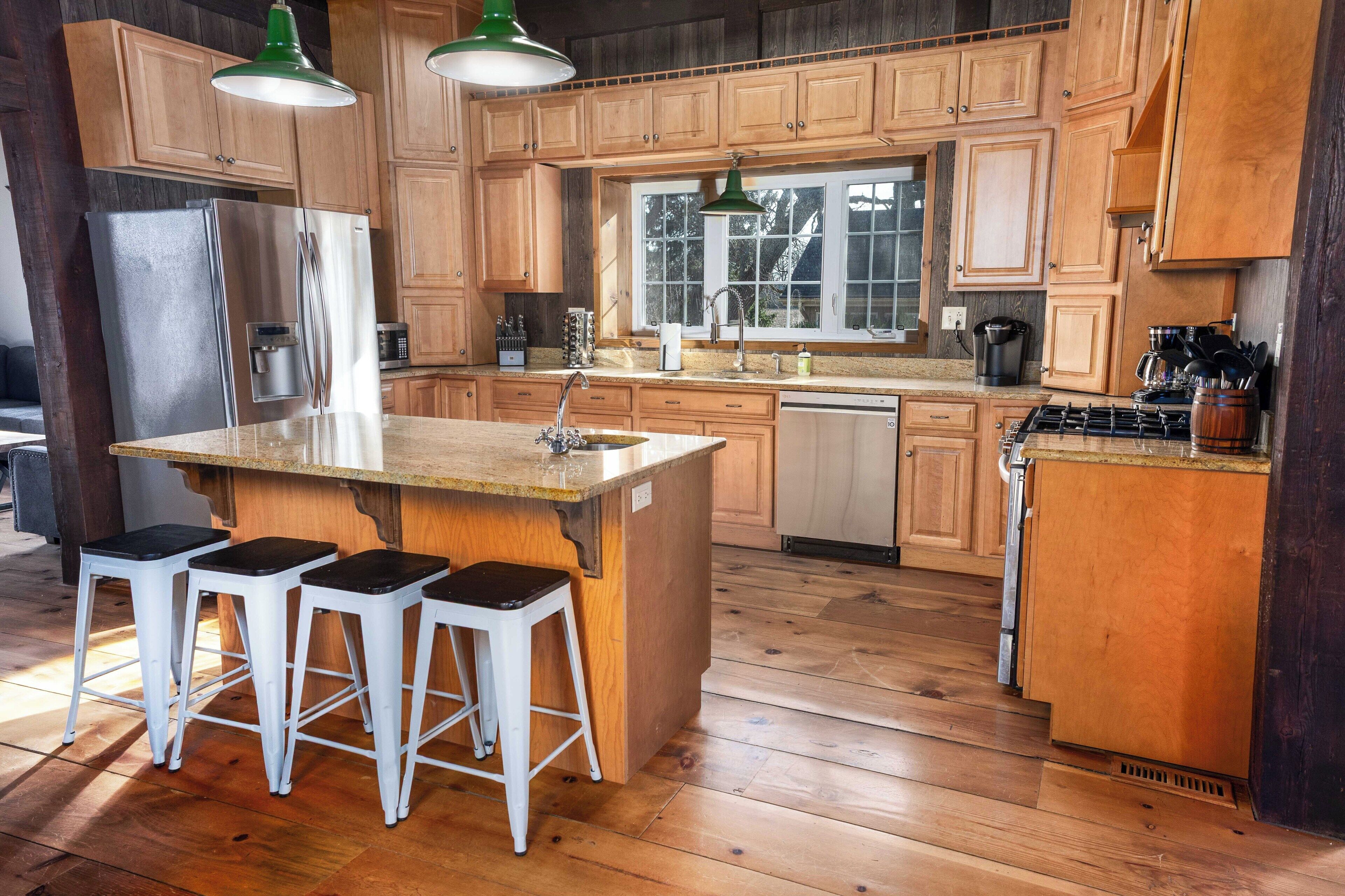 Une cuisine avec des meubles de rangement en bois, un réfrigérateur en acier inoxydable, un évier, une cuisinière et trois tabourets de bar.