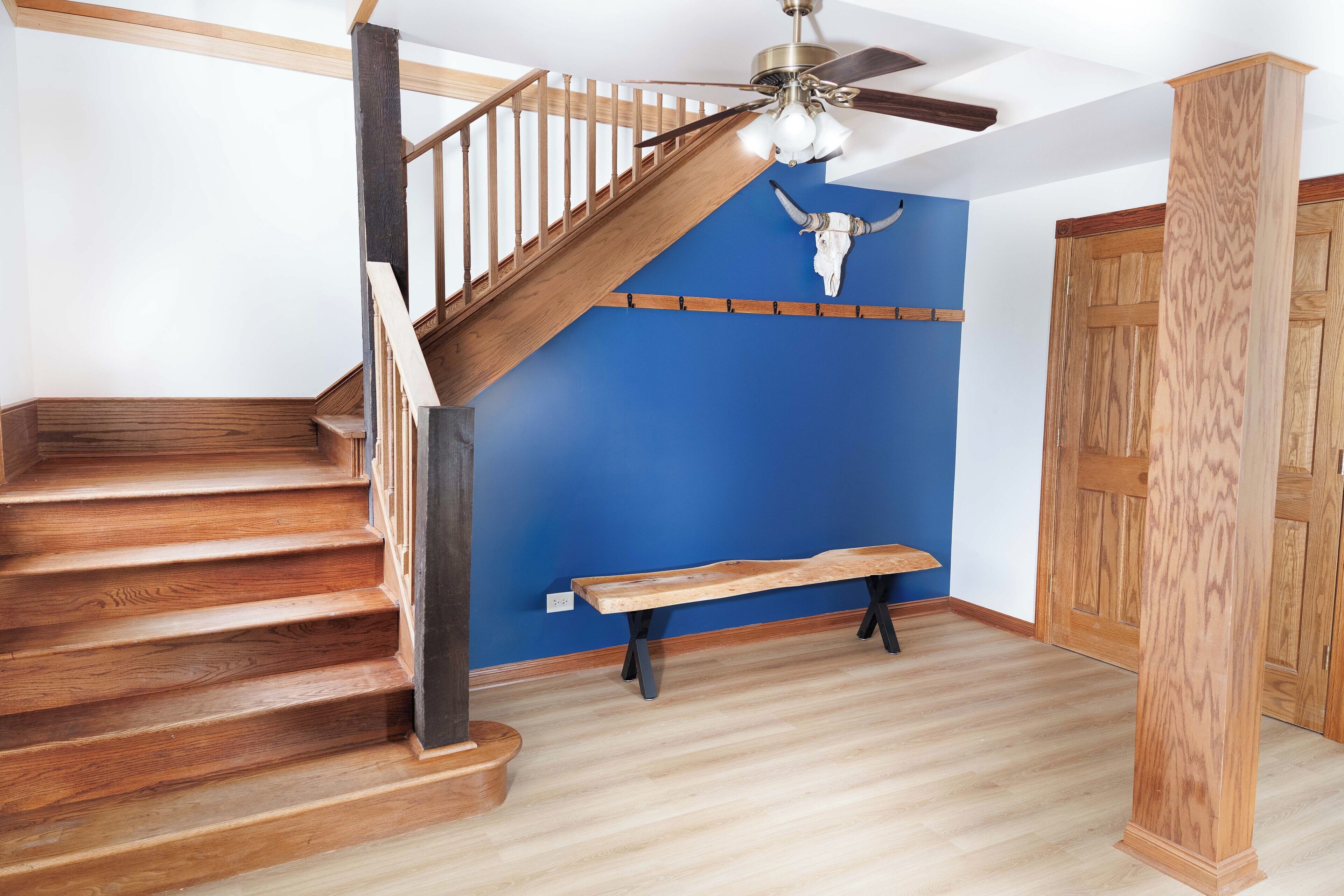 Un escalier en bois, un ventilateur de plafond, un mur d’accent bleu et un banc en bois.