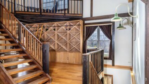 Un escalier en bois mène à une mezzanine agrémentée d’un mur au motif géométrique et d’une fenêtre avec des rideaux.