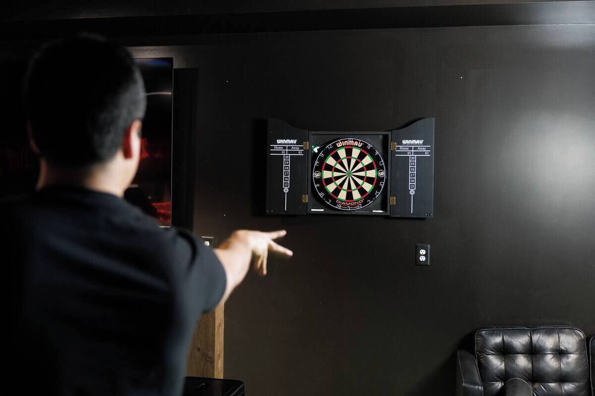 A person playing darts in a room with a dartboard mounted on the wall.