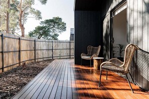 A wooden deck with two wicker chairs, a dark wall, and a metal gate. - Villa 1 | Greenstone Villas (Break O'Day)