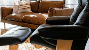 Een moderne woonkamer met een bruine leren bank, een zwarte lederen fauteuil en een houten salontafel.