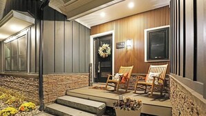Une entrée moderne avec une façade en bois, deux chaises en bois à l’extérieur, un paillasson et une enseigne indiquant l’adresse.