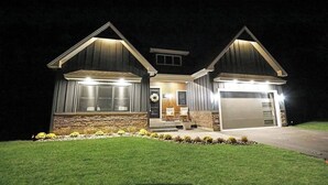 Une maison à deux étages avec des fondations en pierre, un porche à l’avant doté d’un banc et un garage.