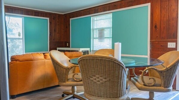 A room with a teal-colored wall, a brown leather sofa, wicker chairs, and a glass table. - Gpl 2668 3 Bed 2 Bath (Fort Myers)