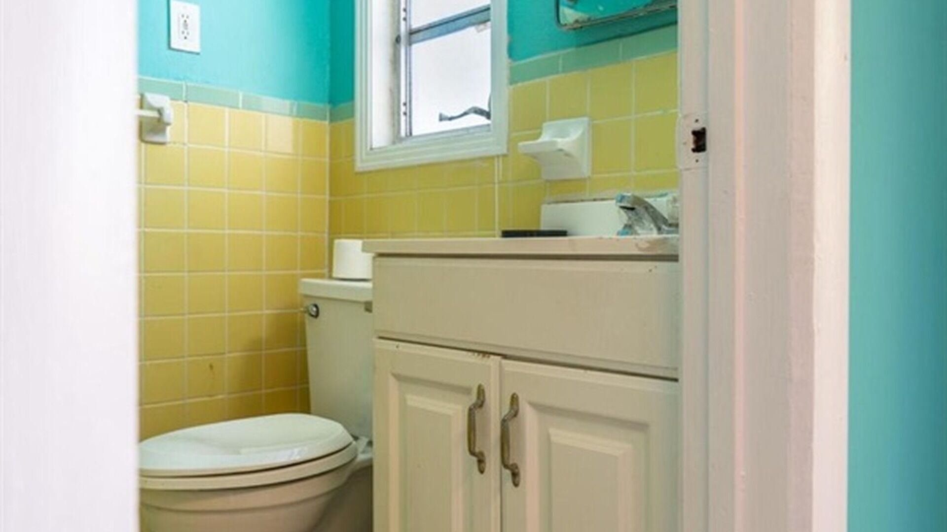 A bathroom with yellow and white tiles, a toilet, and a cabinet with handles.