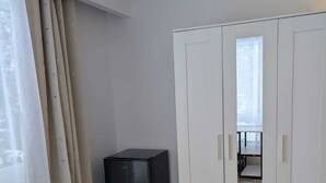 A room with a wooden floor, white walls, a black refrigerator, and a white wardrobe with mirrored doors.