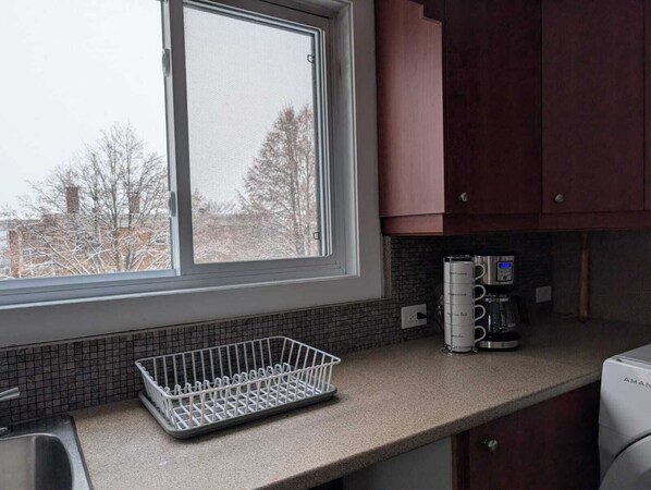 A kitchen with a window, a coffee maker, and a dish rack. - Private Room - 5 min away - University - High-Speed WiFi (Trois-Rivières)