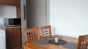 A dining area with a wooden table, four chairs, and a microwave in the kitchen.