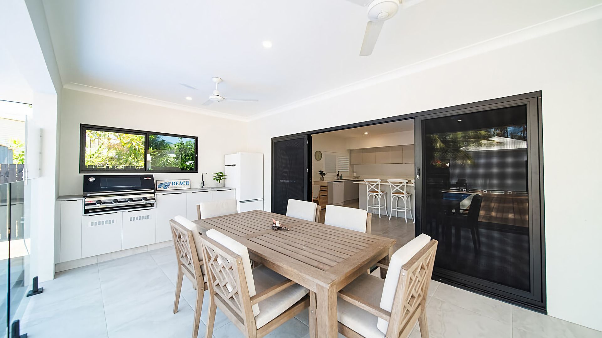 A modern kitchen with a built-in grill, a dining area with a wooden table and chairs, and a sliding glass door leading to a patio.