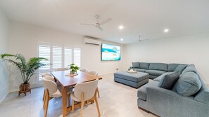 A modern living room with a grey sofa, a wooden dining table with chairs, a potted plant, and a ceiling fan. - Golden Tides - Mission Beach (Mission Beach)