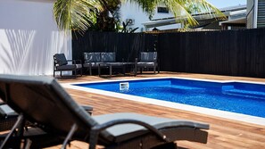 A swimming pool with a wooden deck, surrounded by a black fence, and two lounge chairs. - Golden Tides - Mission Beach (Mission Beach)