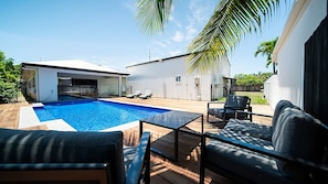 A modern outdoor pool area with a wooden deck, lounge chairs, and a white building with a covered patio. - Golden Tides - Mission Beach (Mission Beach)