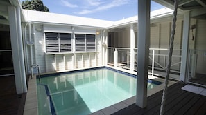 En overdækket swimmingpool med træterrasse, metalstige og glasgelænder.