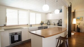 Eine moderne Küche mit einer zentralen Kochinsel, einem eingebauten Backofen und einem Essbereich mit einem Holztisch und Hockern.