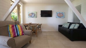 A living room with a sofa, a black couch, a dining table with chairs, and artwork on the walls. - Windjana Wongaling Beach (Wongaling Beach)