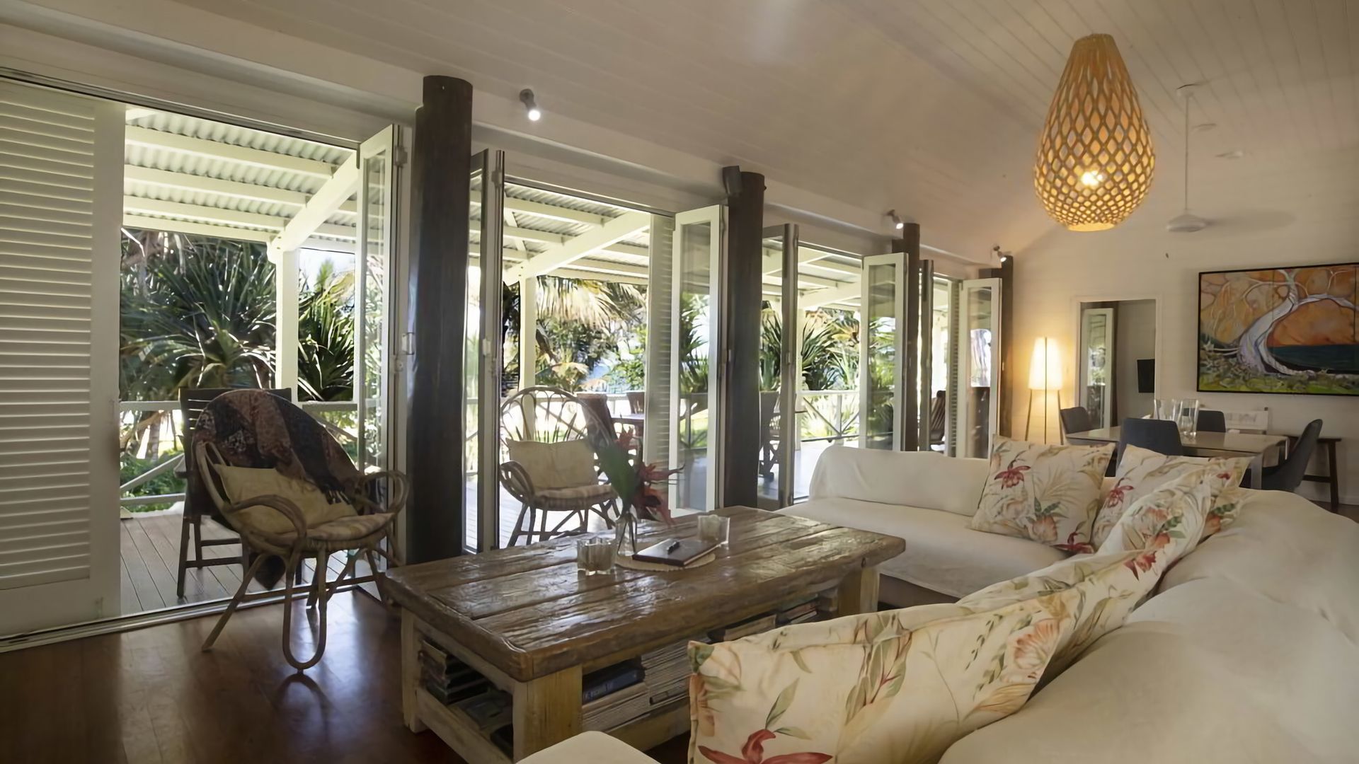 A spacious living area with a sofa, coffee table, and chairs, large windows, and a ceiling fan.