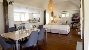 A hotel room with a dining area, a bed with a white duvet, a television, and a large window. - Windjana Wongaling Beach (Wongaling Beach)