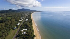 A coastal residential area with a beachfront, houses along the road, and a mountain in the background. - Windjana Wongaling Beach (Wongaling Beach)