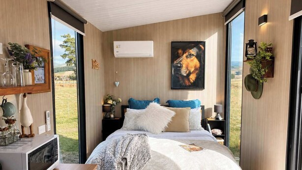 Une chambre à coucher comprenant un lit, des tables de chevet, un climatiseur fixé au mur, un tableau encadré et une vue sur l’extérieur.