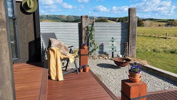 A wooden deck with a chair and a blanket, a metal gate, and a gravel path leading to a field.