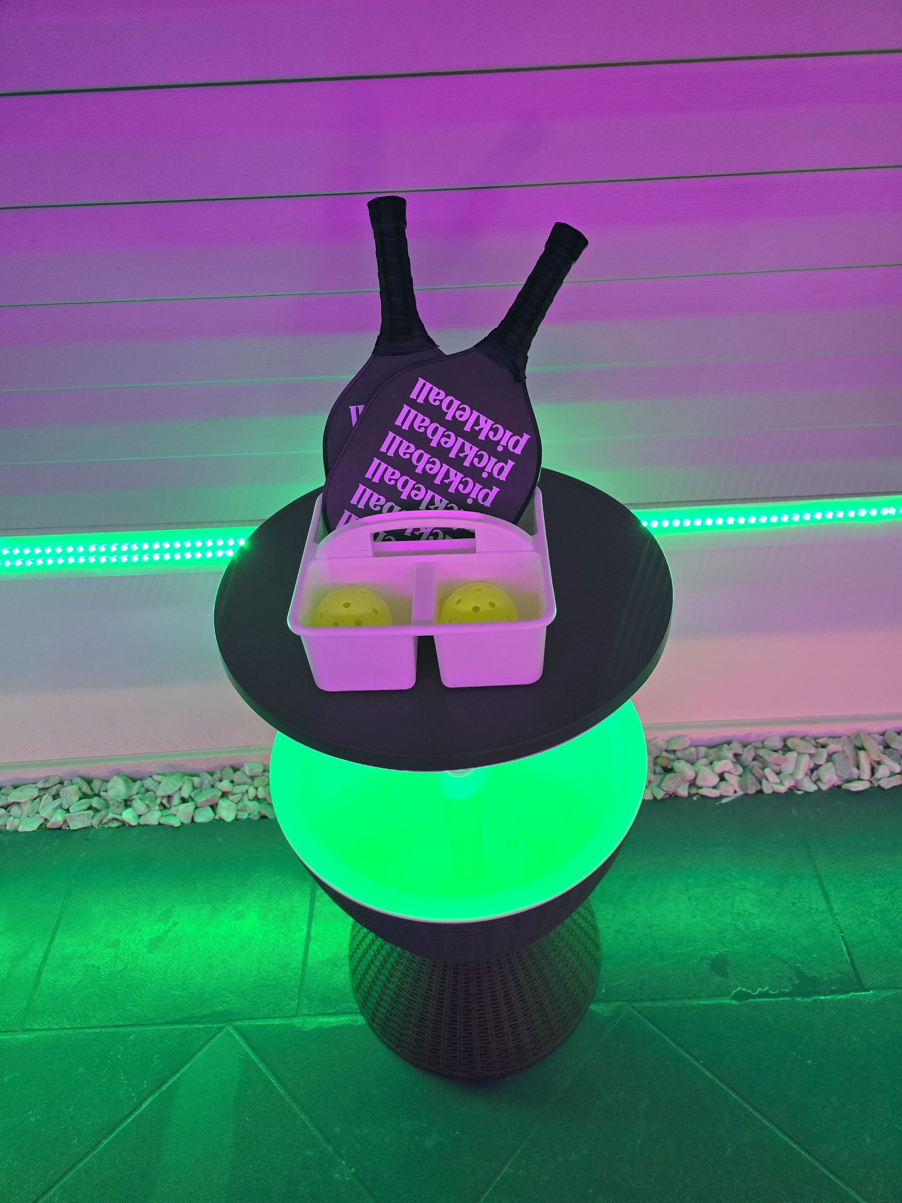 A table with a black object on top, a purple container with text, and a green light underneath.