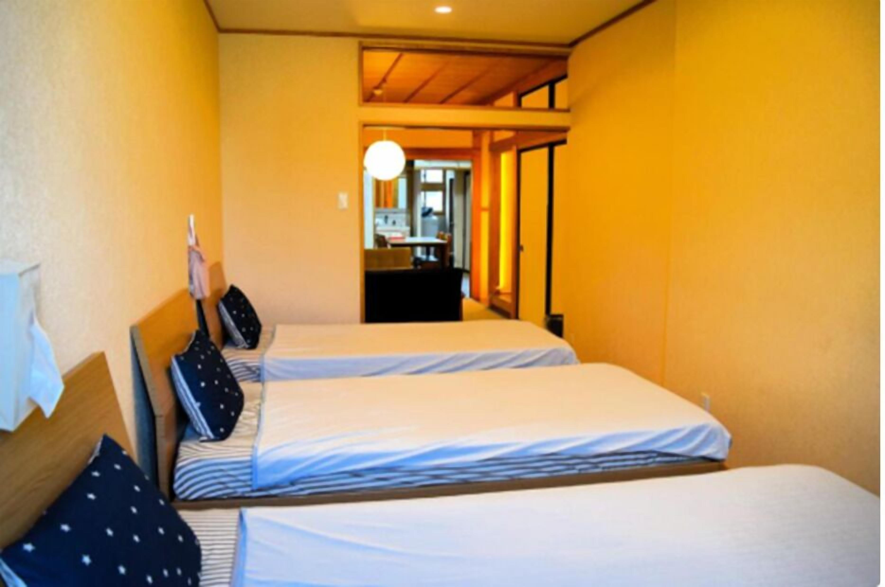A hotel room with two beds, a wooden ceiling, and a view of a dining area.