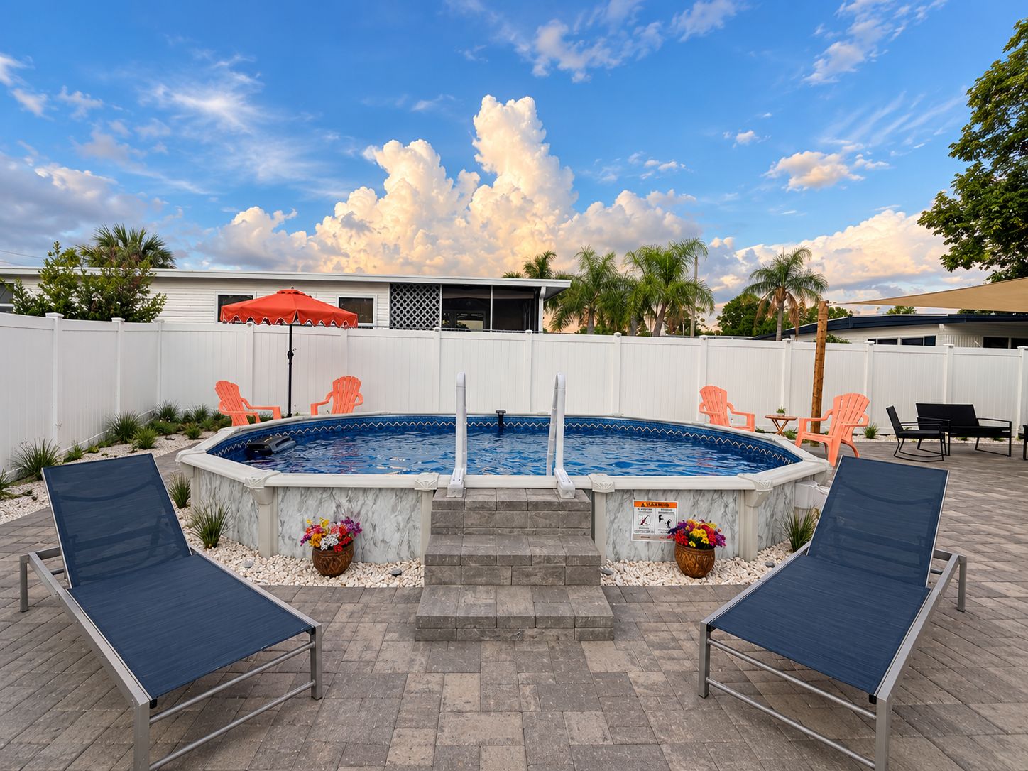 A backyard with a swimming pool, two lounge chairs, a red umbrella, and a white fence.