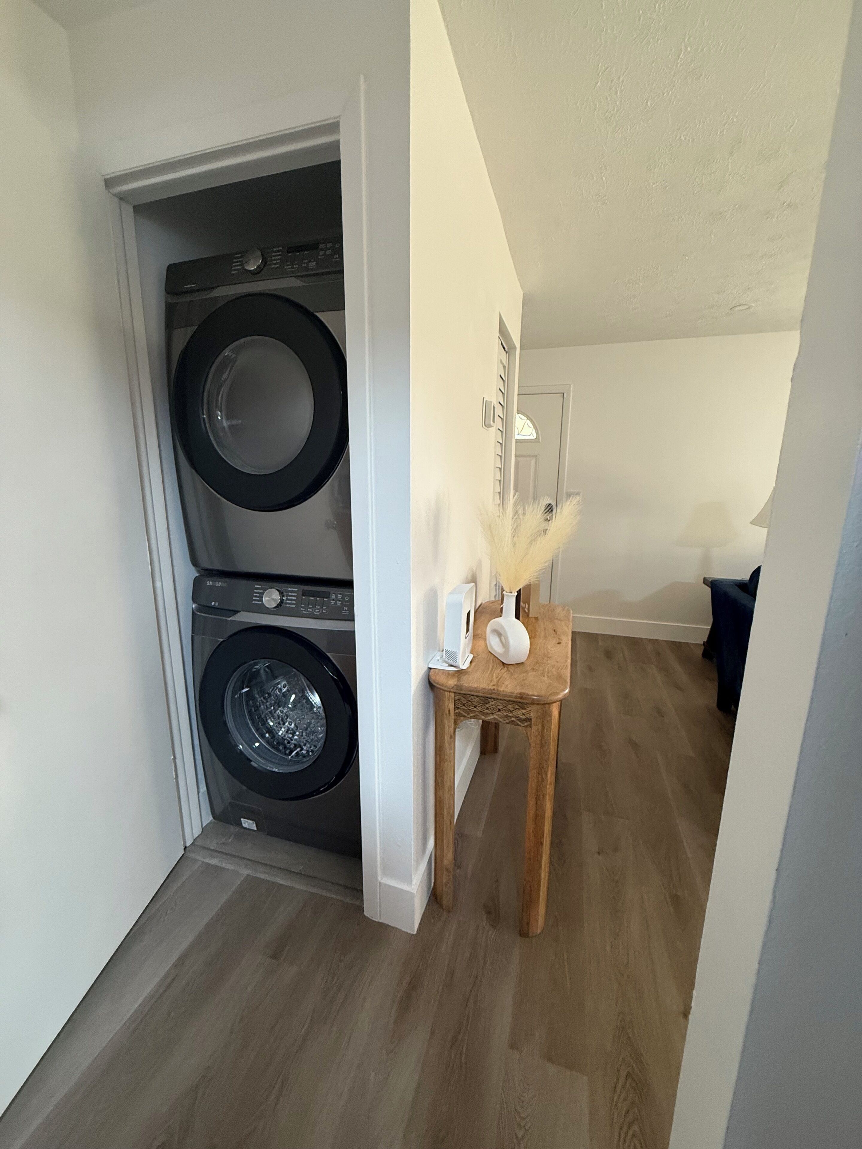 A laundry room with two stacked washing machines and a small wooden table with a lamp and decorative items.