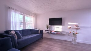 A modern living room with a blue sofa, a flat-screen TV mounted on the wall, and a decorative vase with dried flowers. - Sunny Oasis by Tarpon - Heated Pool, Hot Tub & Playground (Holiday)