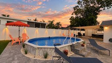 A backyard with a swimming pool, lounge chairs, and a patio area.