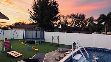 Un jardin avec une piscine, un trampoline et une balançoire.