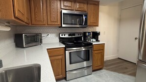A kitchen with wooden cabinets, a stainless steel microwave, a toaster, a stove, and a refrigerator. - Sunny Oasis by Tarpon - Heated Pool, Hot Tub & Playground (Holiday)