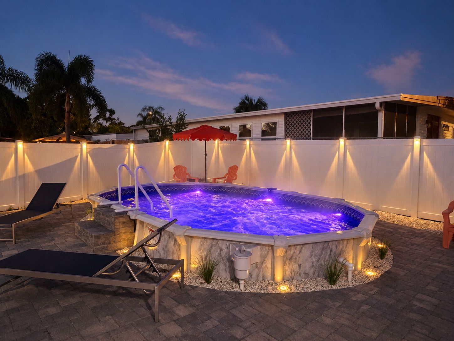 An outdoor swimming pool with a hot tub, surrounded by a white fence, and equipped with outdoor furniture and lighting.