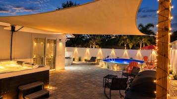 A covered outdoor area with a hot tub, seating, and a swimming pool.