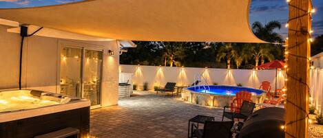 A covered outdoor area with a hot tub, seating, and a swimming pool.