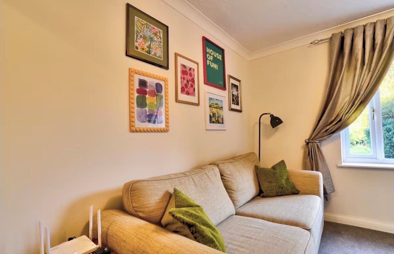 A living room with a beige sofa, green cushions, a white router, and framed artwork on the wall.