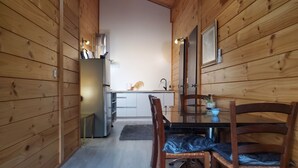 Une cuisine compacte aux murs en bois, équipée d’un réfrigérateur, d’un évier et d’un coin repas avec des chaises et une table.