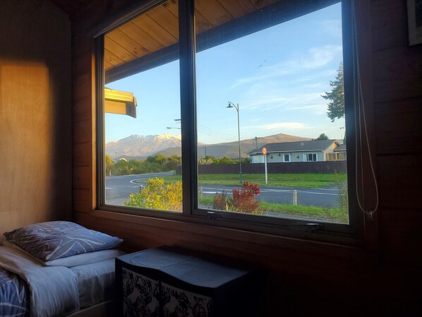 A room with a large window offering a view of a road, a house, and a mountain range.