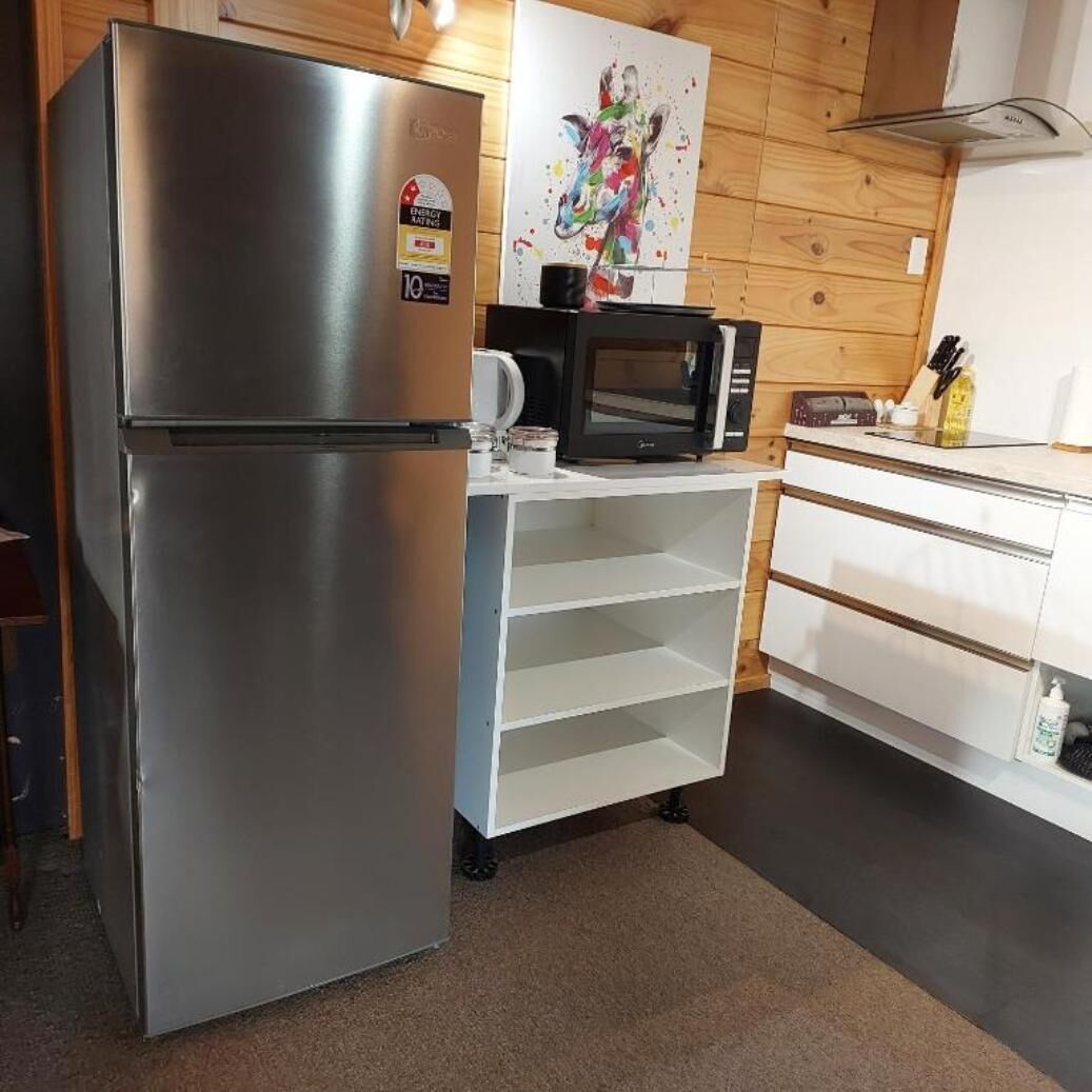 Een kleine keuken met een roestvrijstalen koelkast, een magnetron en een wit kastje met planken.