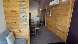 Un intérieur en bois avec un canapé, un coin repas avec des chaises et une cuisine à l’arrière-plan.