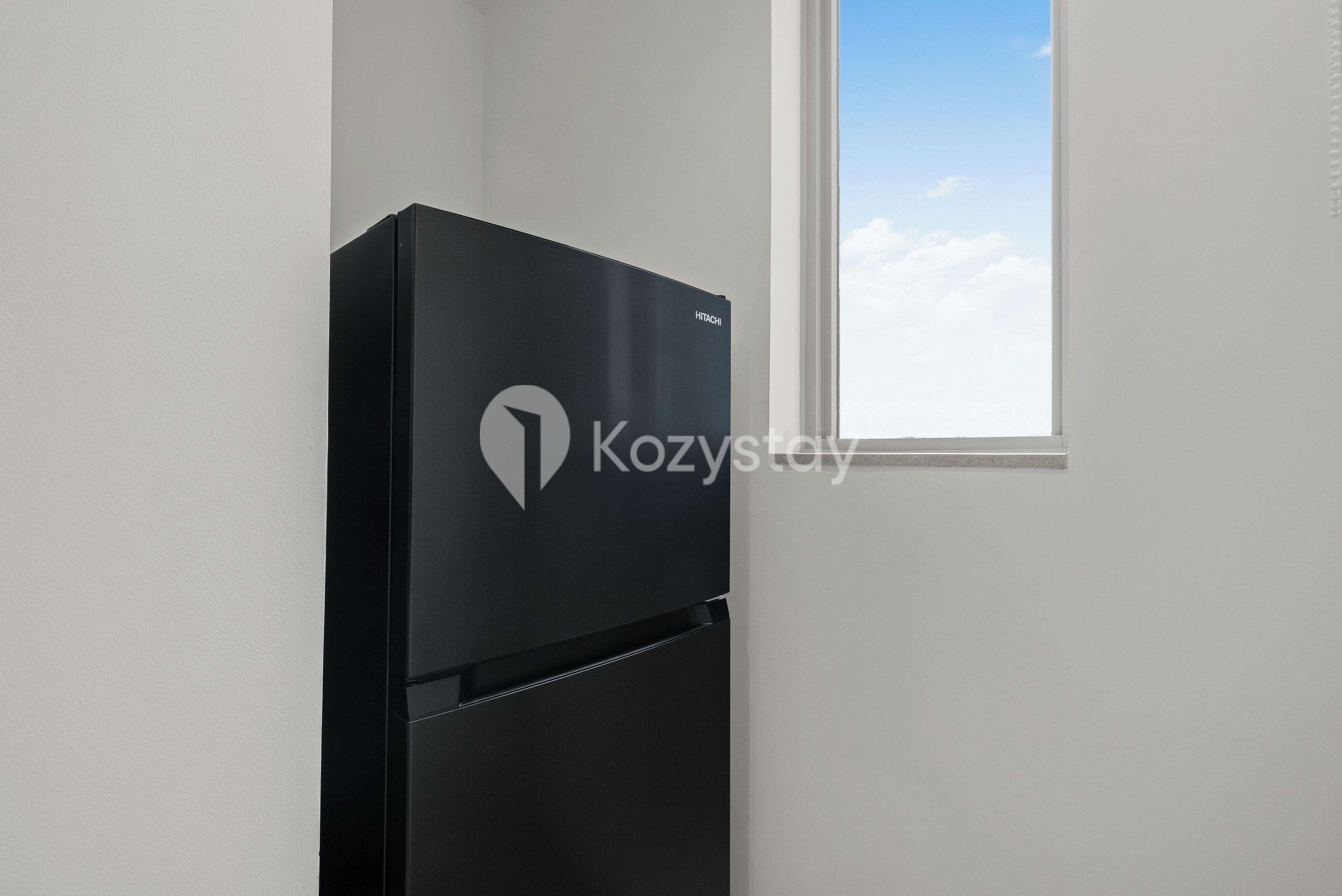 A black refrigerator with a logo in a room with white walls and a window.
