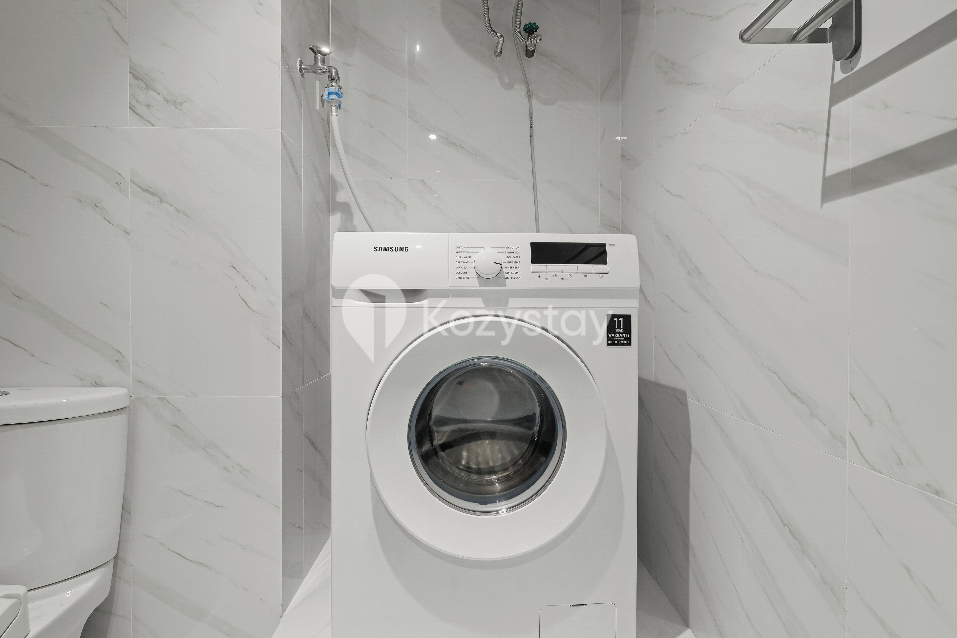 Eine moderne, weiße Waschmaschine in einem Badezimmer mit Marmorwänden und einer Toilette.
