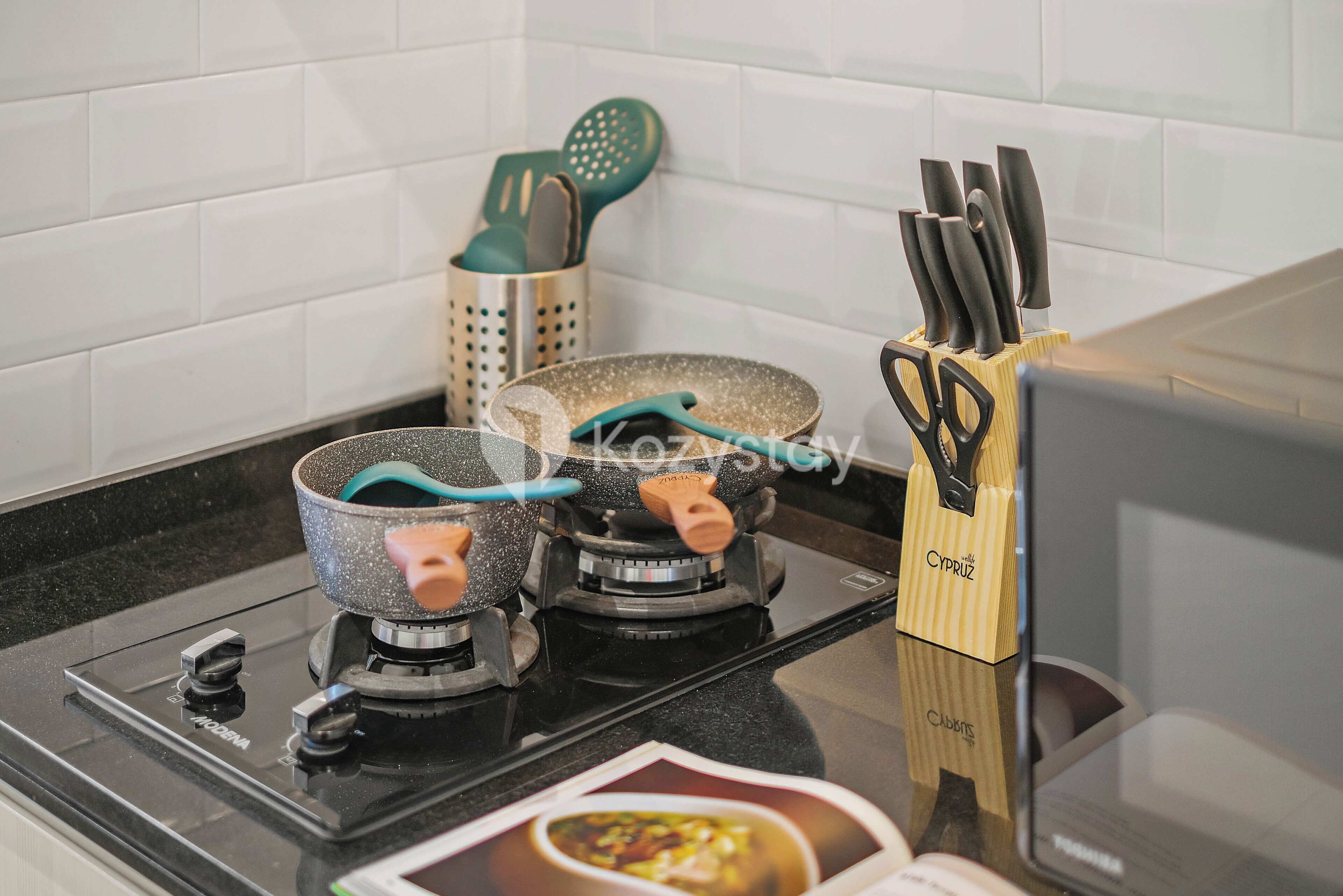 A kitchen with two gas stoves, a pot on one, and a set of kitchen utensils on the counter.