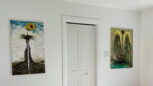 Una habitación con piso de madera, una puerta blanca y dos cuadros en la pared.